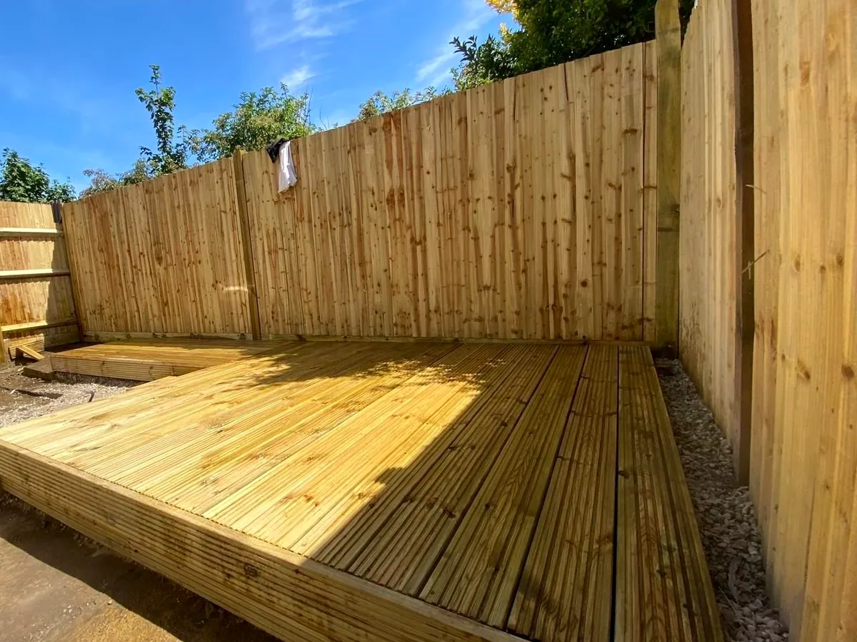 New softwood timber decking laid into a garden corner against feather-edge fencing under a clear sky